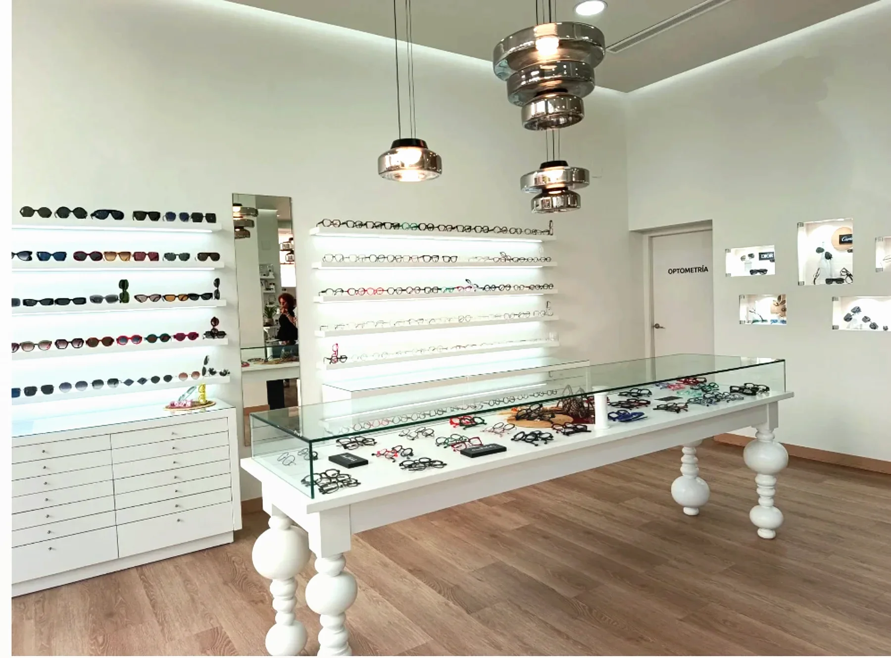 Interior de la óptica Senti2 en Moraira: mesa vitrina con gafas, expositores iluminados y la sala de optometría